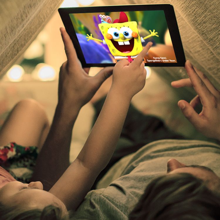 Padre e hijo acostados adentro de una carpa hecha con una manta viendo SpongeBob en una tablet