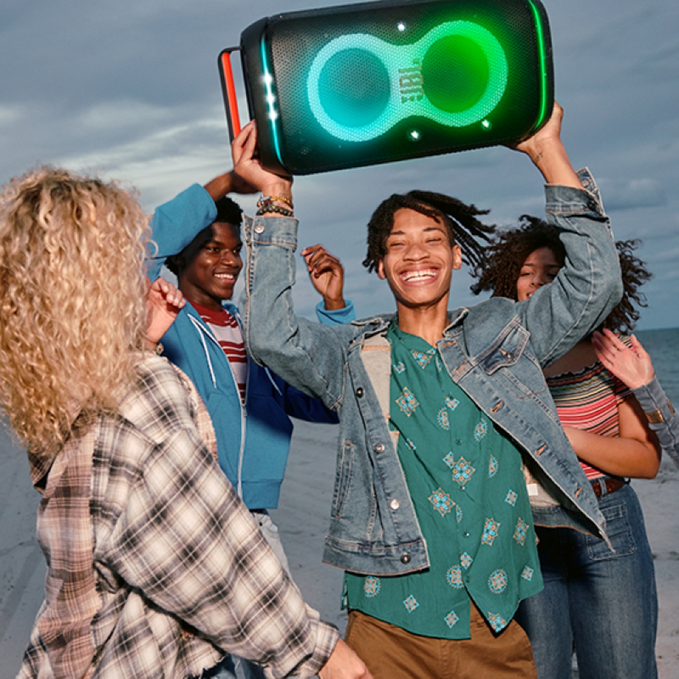 Friends on the beach listening to a JBL PartyBox Club 120