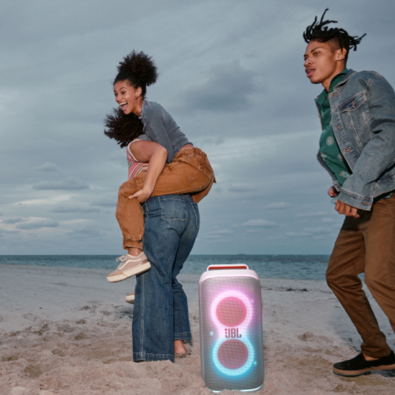 Three friends on the beach listening to a JBL PartyBox Club 120