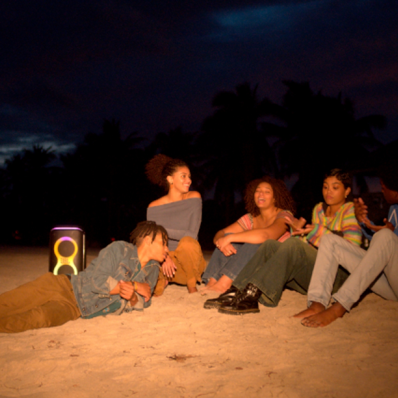 Friends on a beach at night listening to a JBL PartyBox Club 120