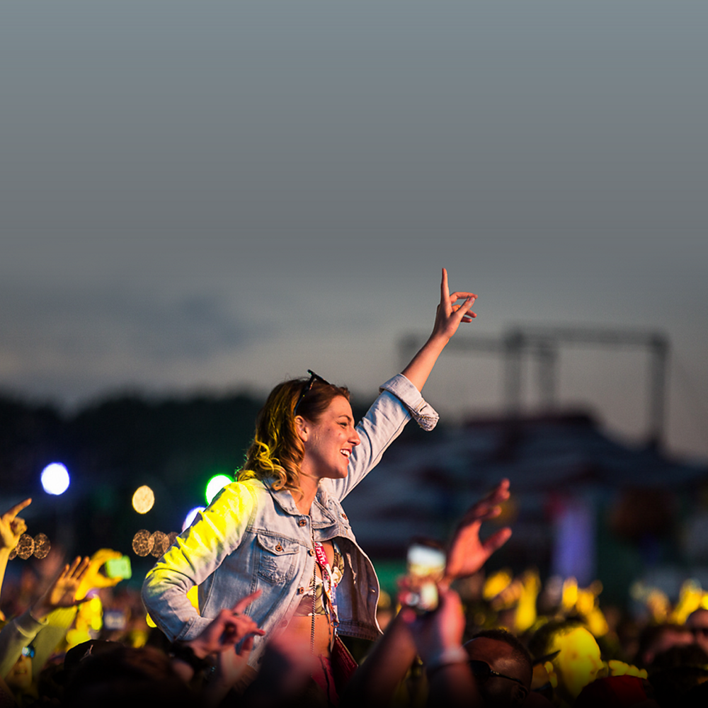 A smiling woman stands with her hand in the air at a concert.
