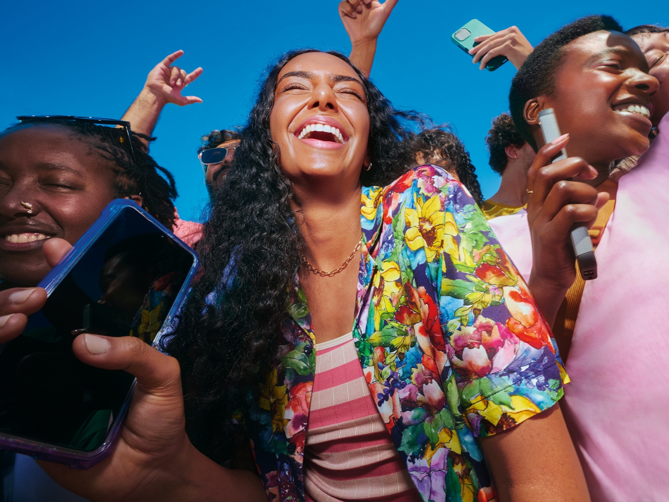 A woman is with a group of friends, smiling as they hold onto their cell phones with their hands. 