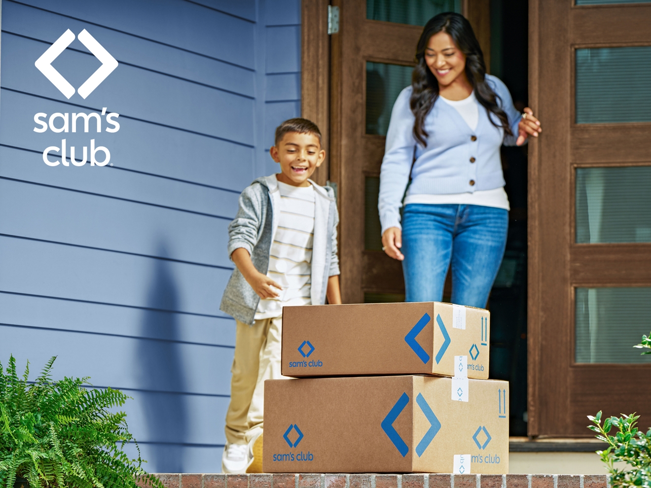 Parent and child excitedly retrieving Sam’s Club boxes that have been delivered to their front porch