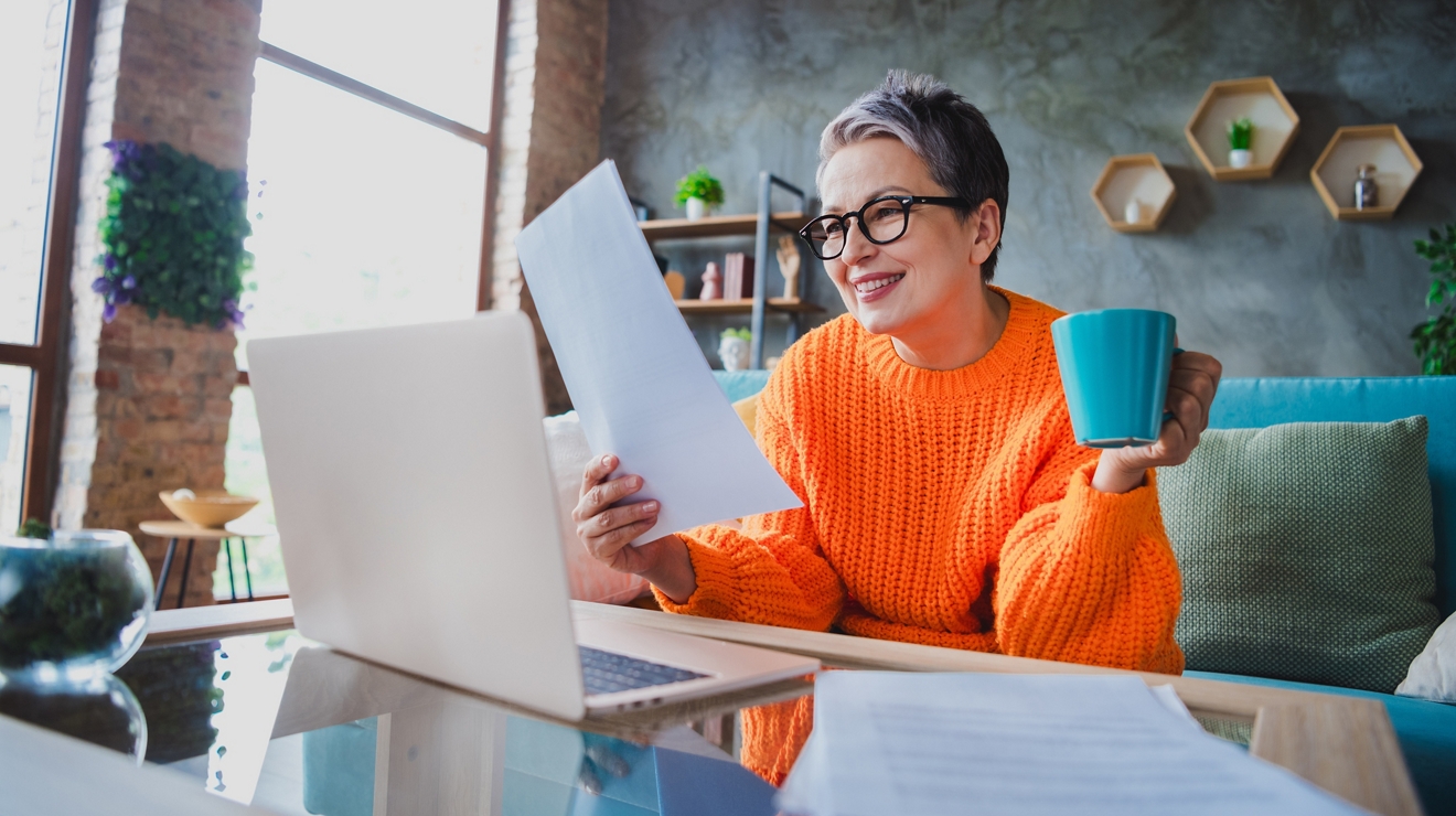 Photo of smiling positive elderly lady wear orange pullover working modern device reading report indoors apartment room; Shutterstock ID 2371415755; Client Name:Jeanette Delgado; Project #:State Relay; Project Name:State Relay; purchase_order:; job: