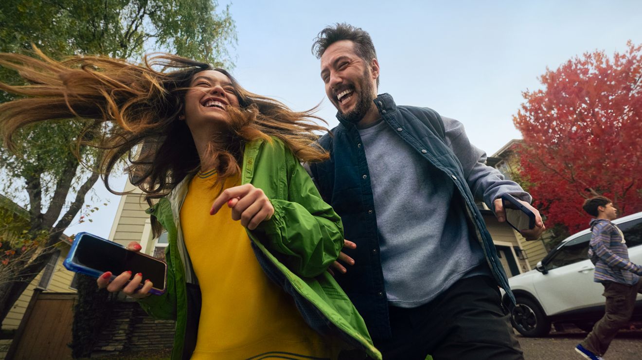 Couple laughing during autumn while a child runs in the background.