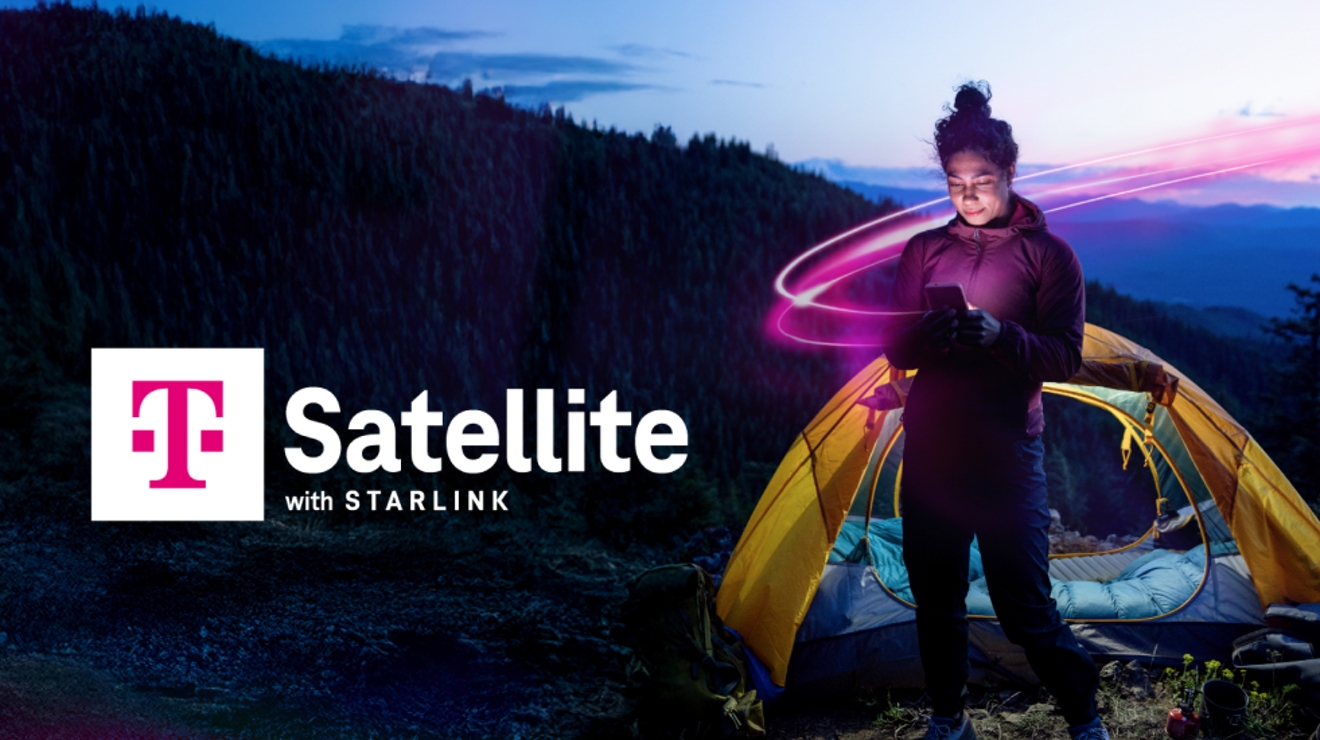 A woman stands outside of her tent in the mountains. She smiles at her glowing phone screen using T-Mobile Satellite with Starlink. Magenta light wraps around her. 