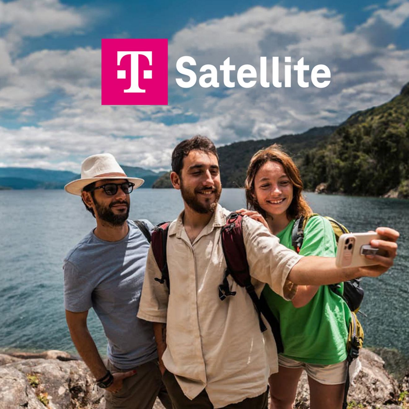 Group of friends taking a selfie on a rocky lakeshore with mountains in the background.
