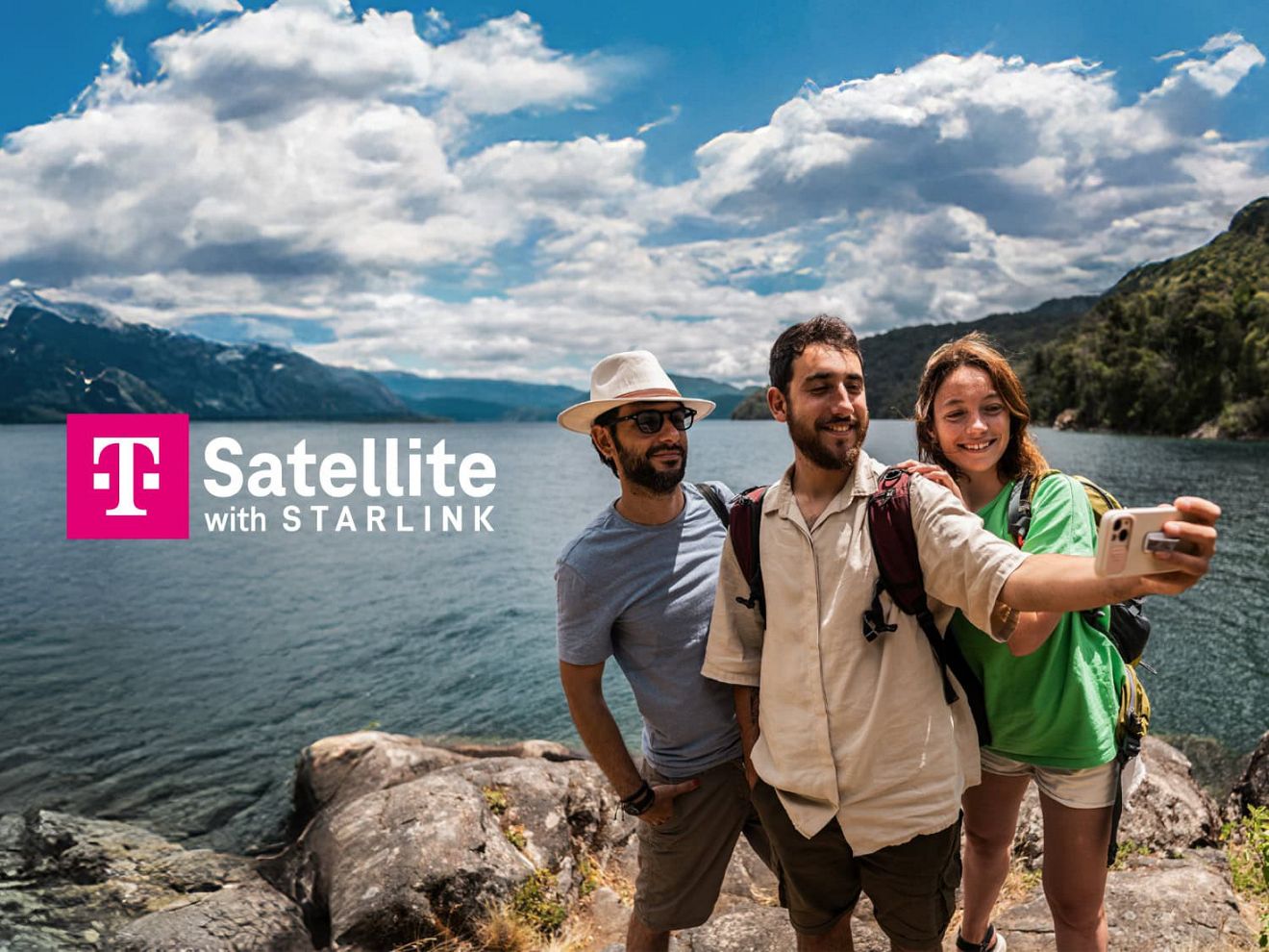 Group of friends taking a selfie on a rocky lakeshore with mountains in the background and “T Satellite with Starlink” text.