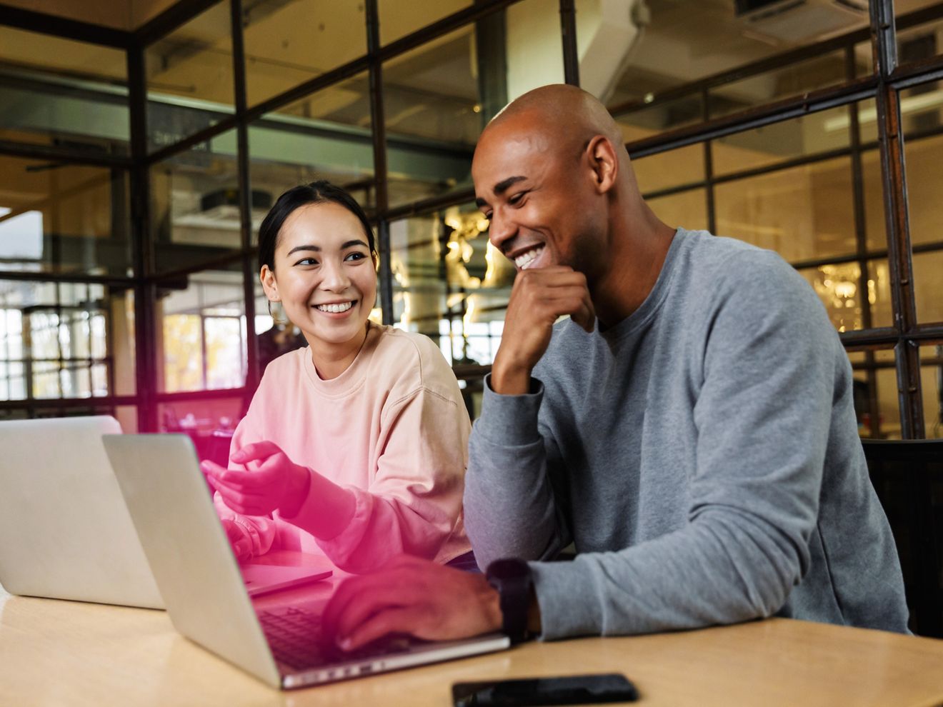 Two work colleagues chat over their laptop screens that glow with T-Mobile magenta beams.