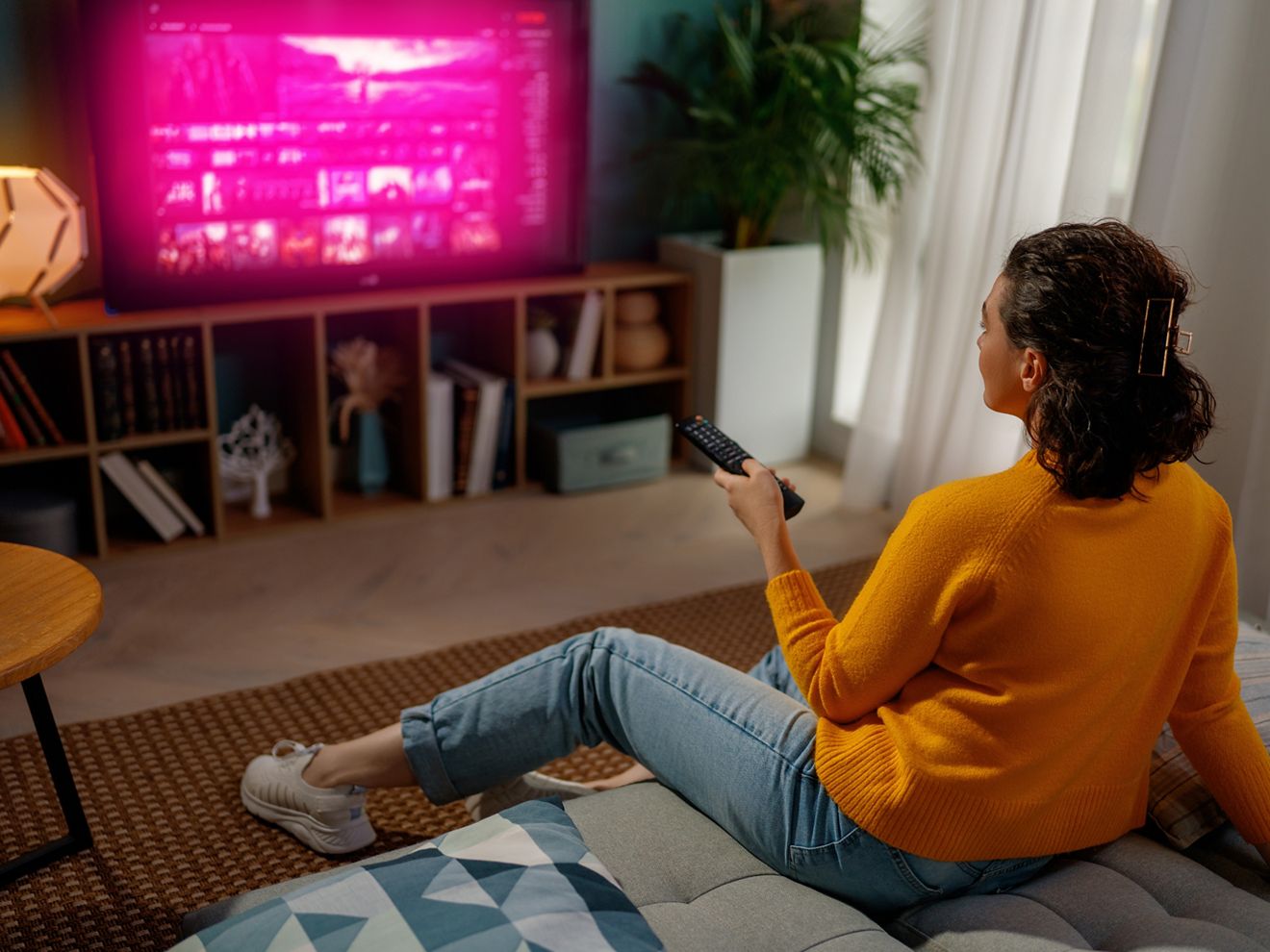 Woman watches TV with T-Mobile magenta glow as she relaxes on the couch in her living room. 