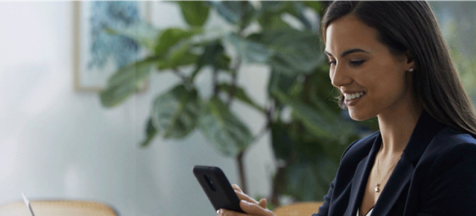 A smiling financial services professional uses her smartphone while seated in a conference room