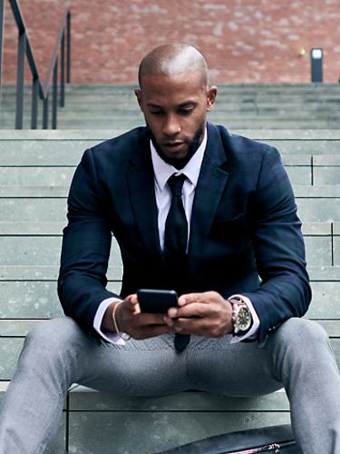 A financial services professional stays connected on his phone while seated on an outdoor staircase