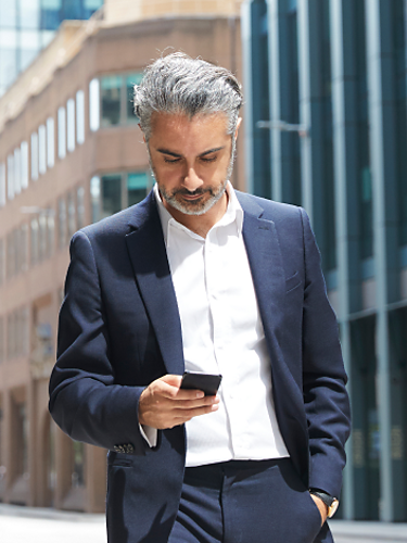 A financial services professional uses his smartphone while walking down the street.