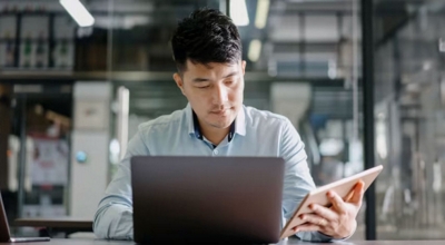 A young professional uses a laptop and tablet simultaneously.