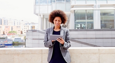 A young professional uses a tablet on an outdoor landing of her office building.