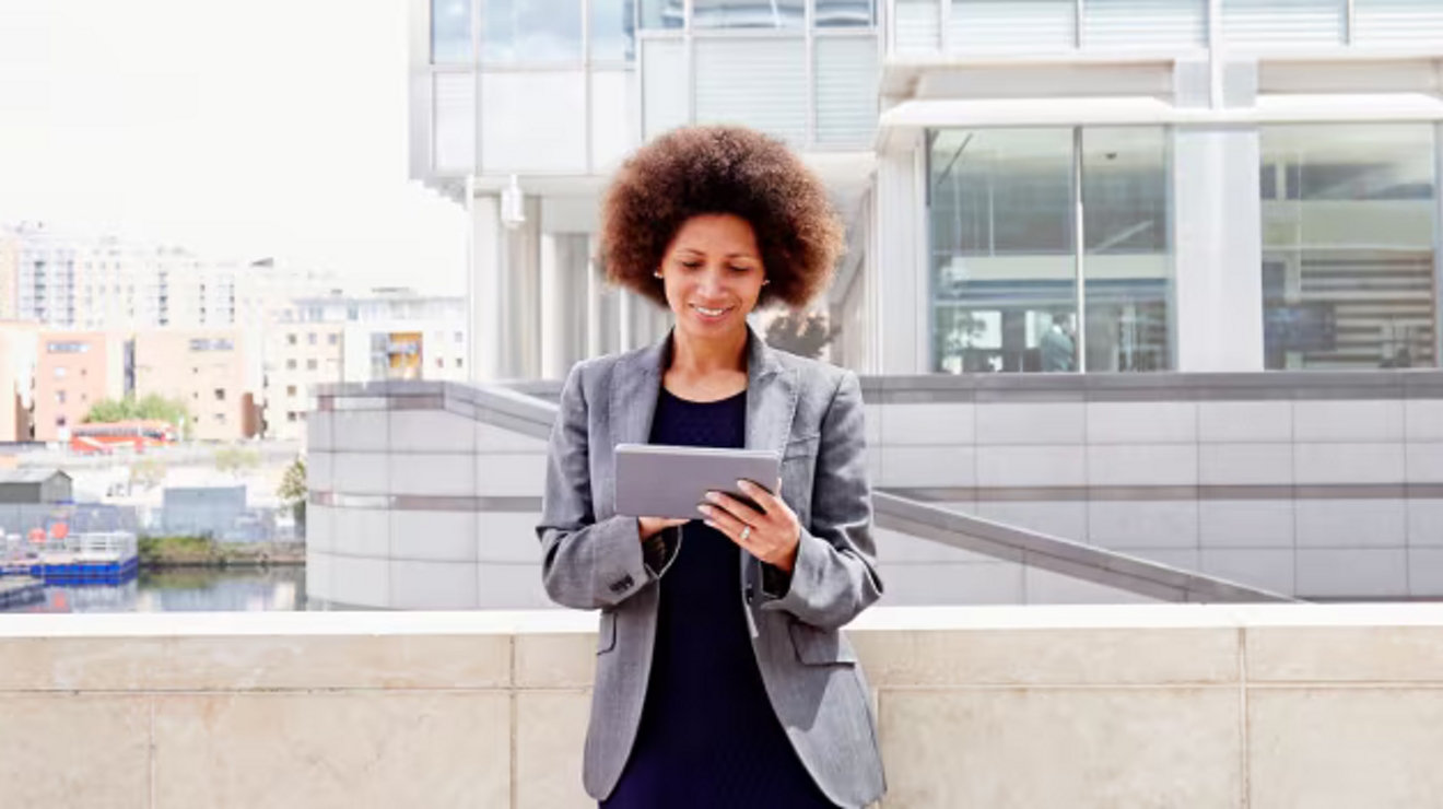 A professional uses a tablet on an outdoor landing of an office building.