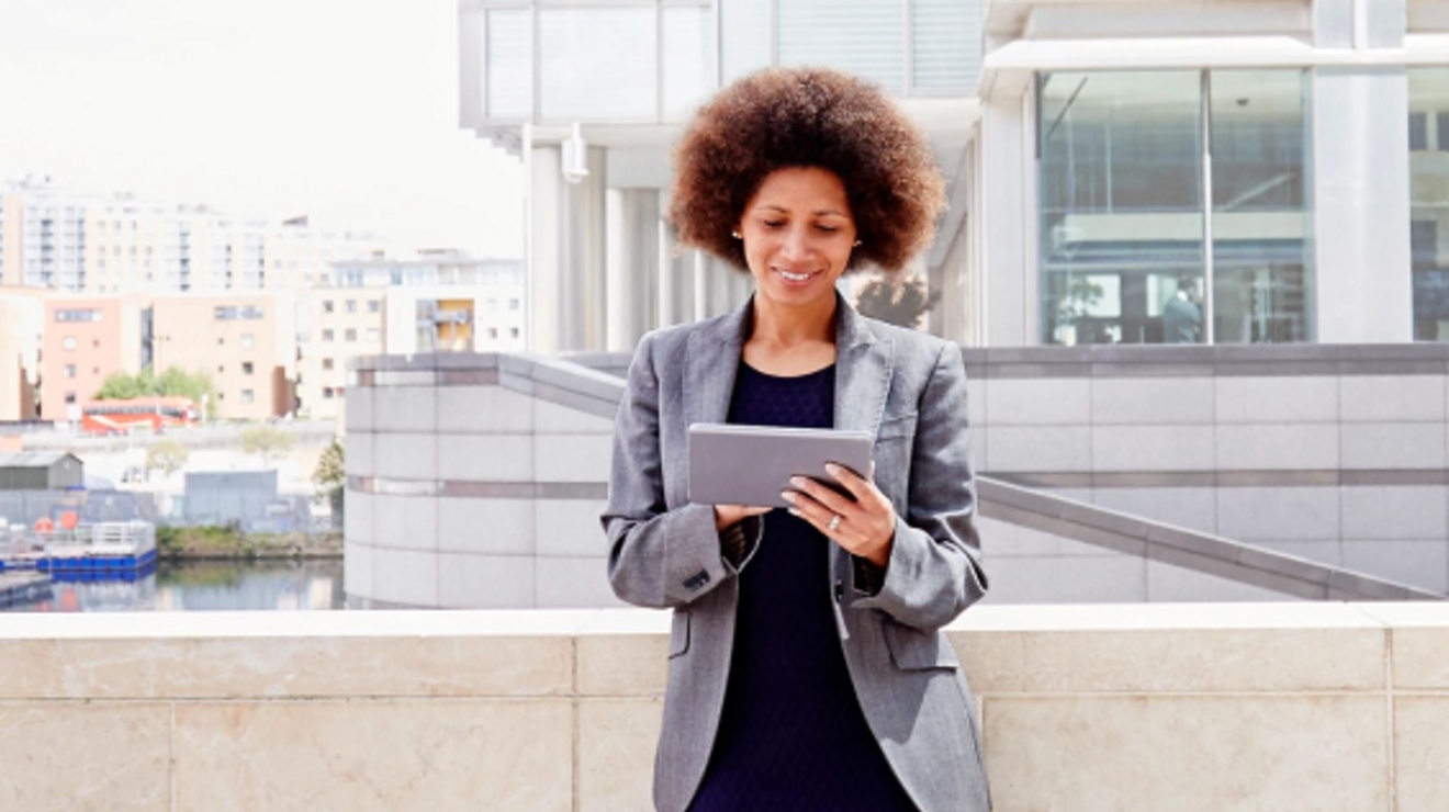A young professional uses a tablet on an outdoor landing of her office building.