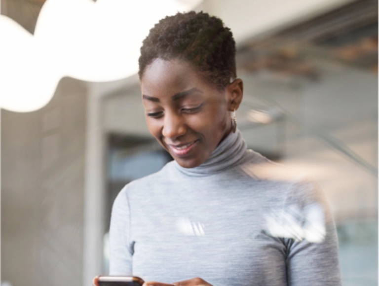 A young worker smiles at her phone while standing at a worksite