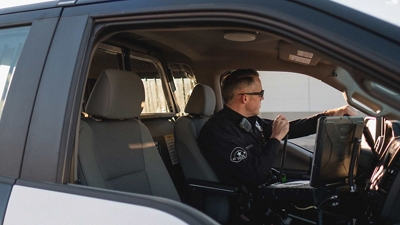 An officer in the driver seat of a patrol car speaks over a radio.