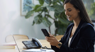 A smiling financial services professional uses her smartphone while seated in a conference room.