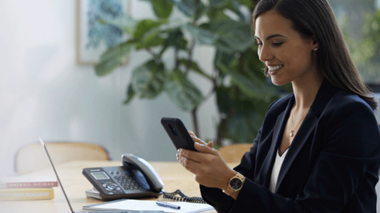A smiling financial services professional uses her smartphone while seated in a conference room.