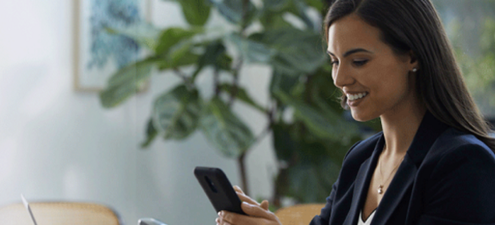 A smiling financial services professional uses her smartphone while seated in a conference room.