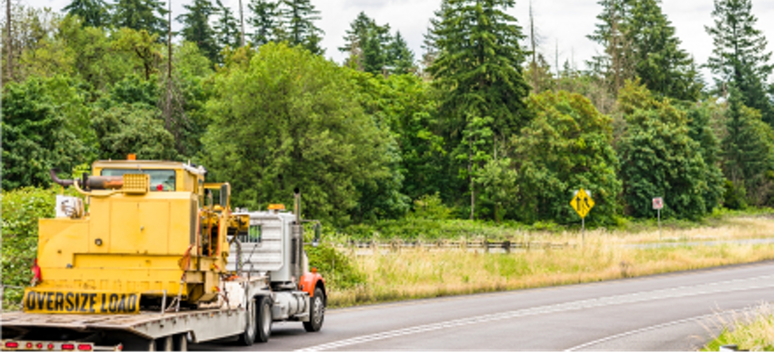A semi-truck carrying an oversized load on a curved highway.