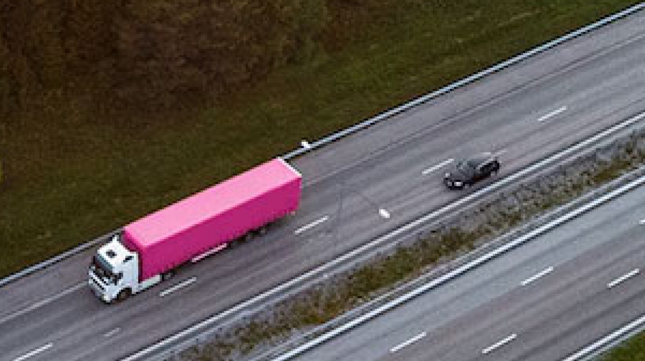 Overhead view of a highway and a magenta semi-truck with trailer.