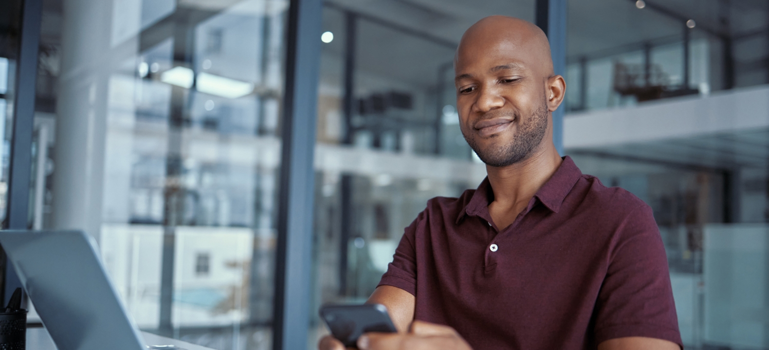 A young professional uses his smartphone and laptop while working from home. 