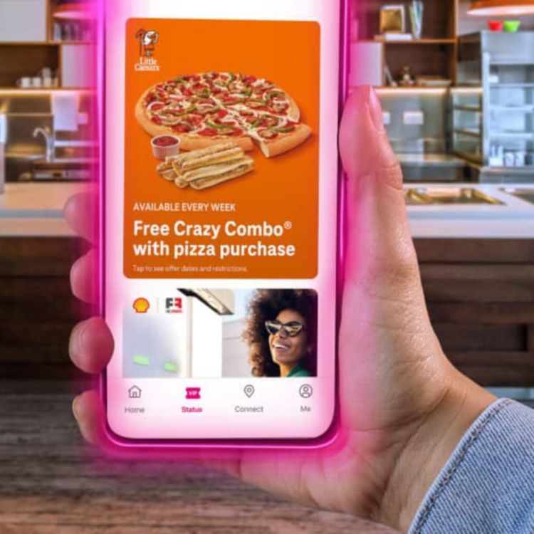 A pizza combo offer shown on a smartphone screen held in front of a restaurant counter.