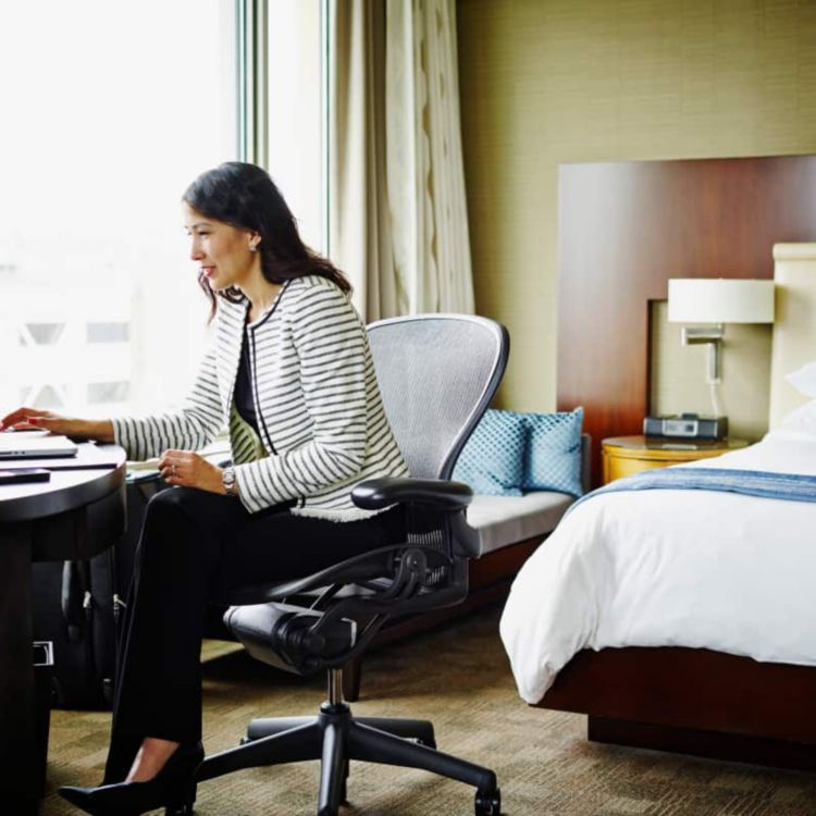 A professional traveling on business works on her laptop while seated in her hotel room.