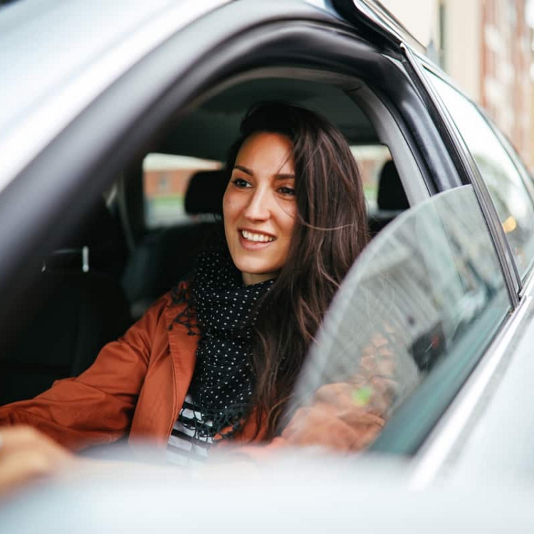 A smiling woman drives a rental car with the window down.