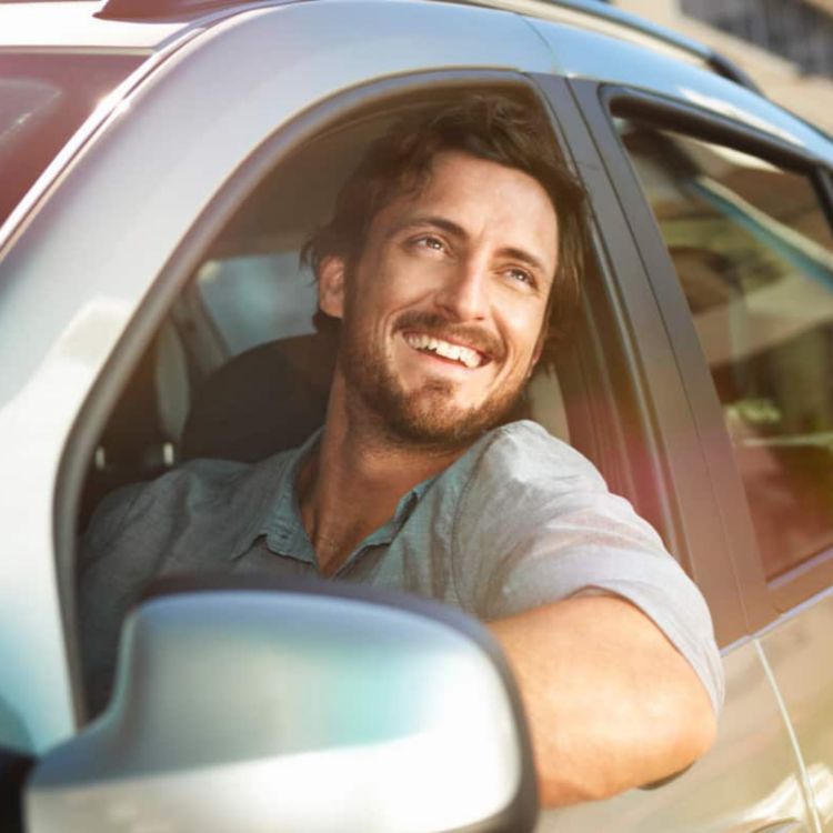 A smiling man looks out the window while driving a rental car.