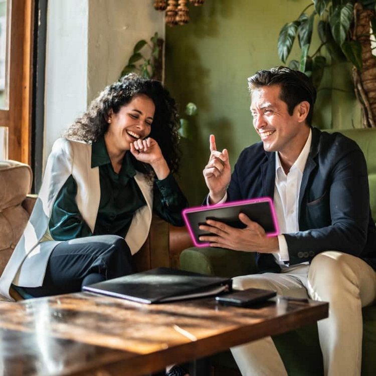 Two people laugh while looking at a tablet.