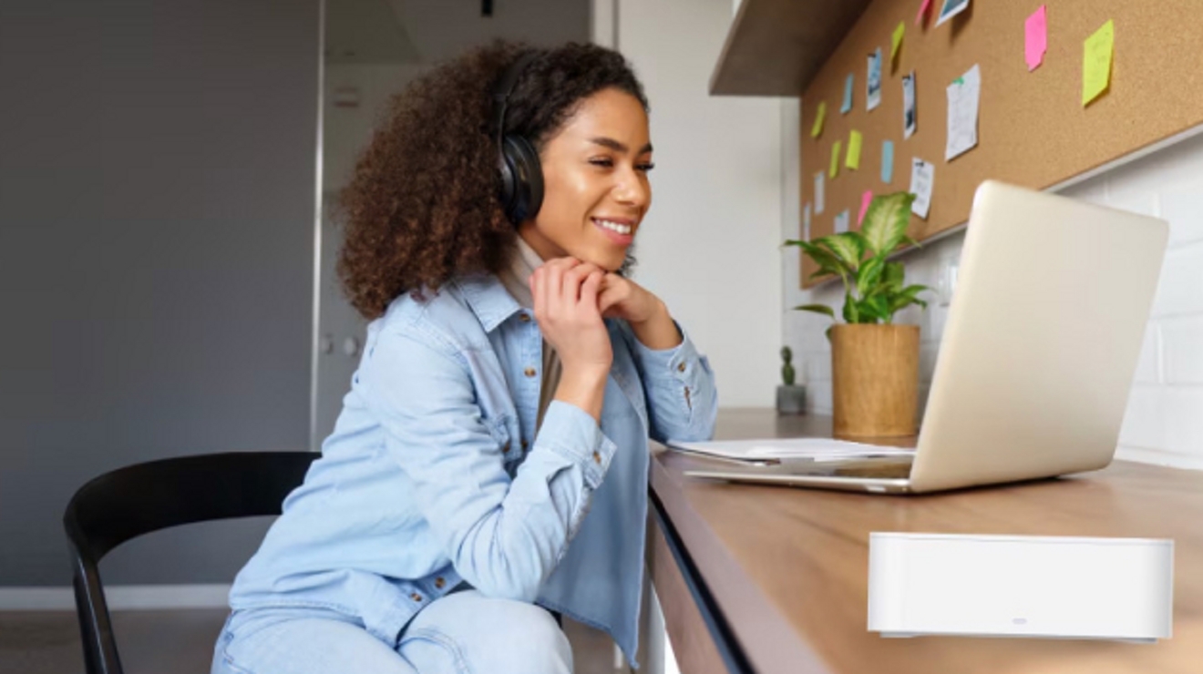 Student wearing headphones sits at a desk and smiles at her laptop screen.