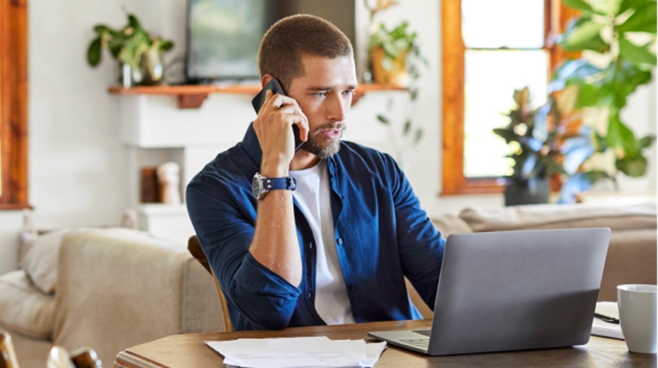 A young professional uses his smartphone and laptop while working from home.