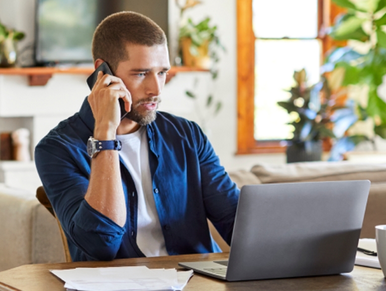 A young professional uses his smartphone and laptop while working from home.