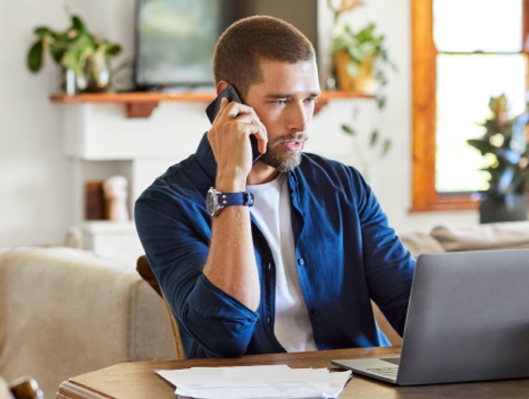 A young professional uses their smartphone and laptop while working from home.