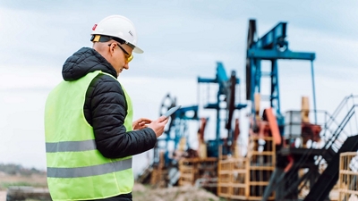A professional wearing protective gear works with a tablet at a drilling site.