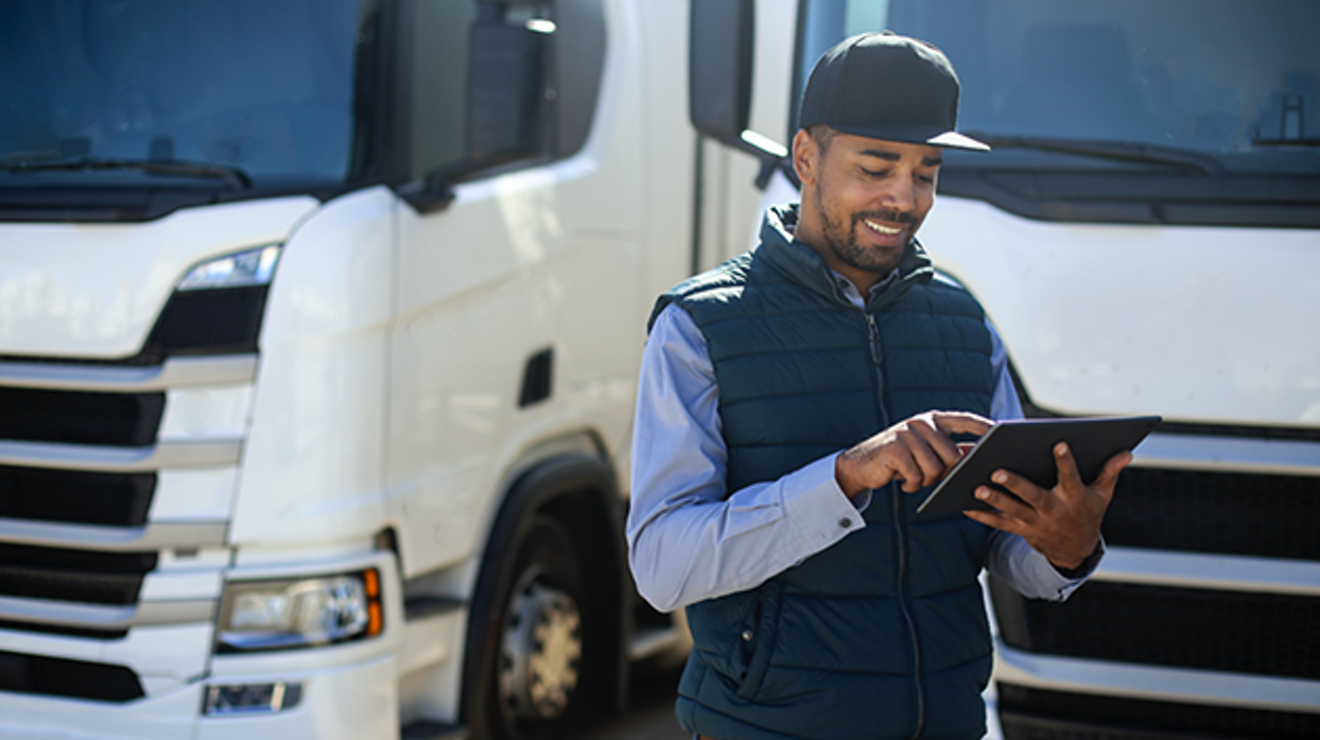 Smiling person uses a tablet while standing in front of parked two semi-trucks.