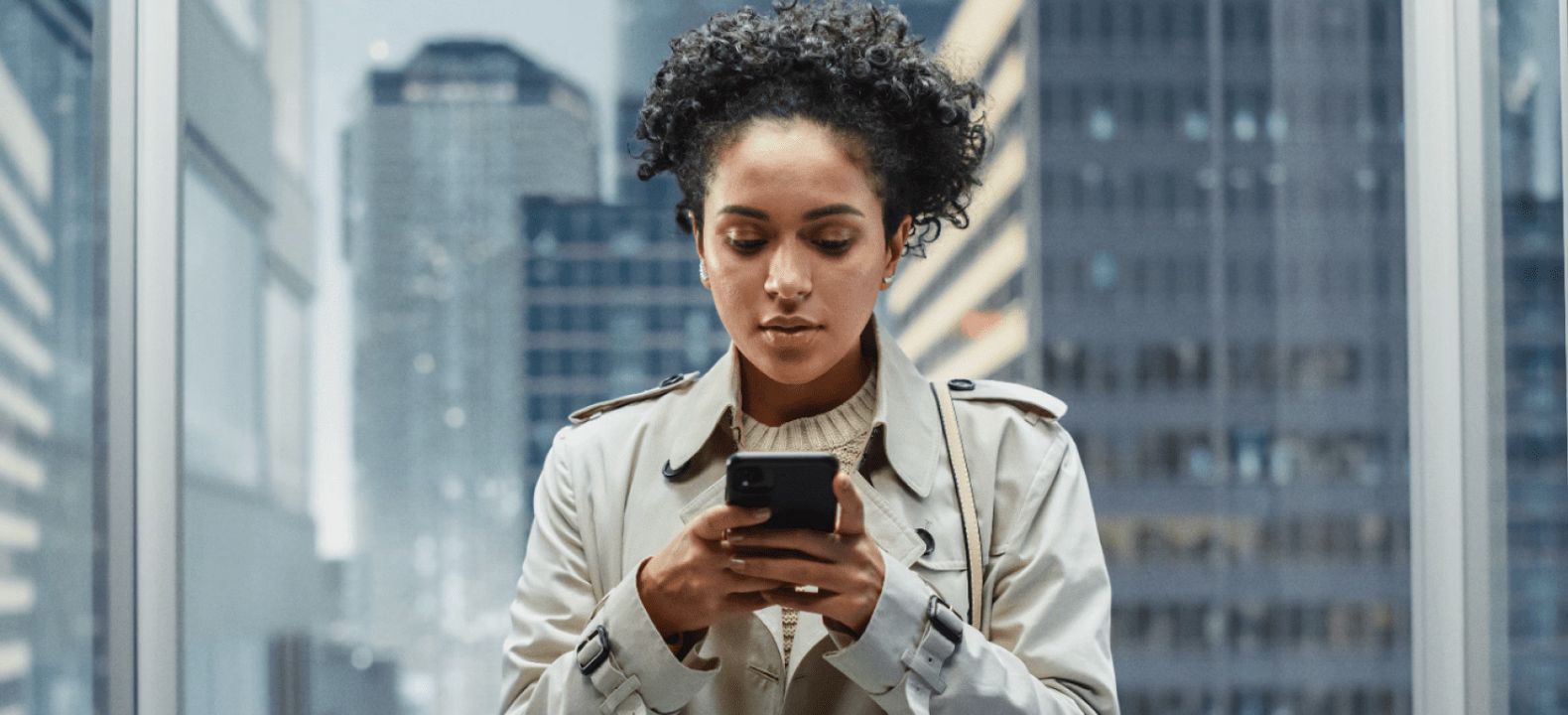 A young financial services professional on her smartphone in an urban glass office building.