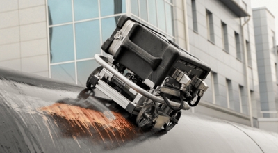 A robot rolls along the side of a building.