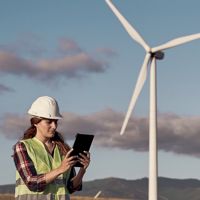 A female engineer holding a tablet with a windmill in the background.