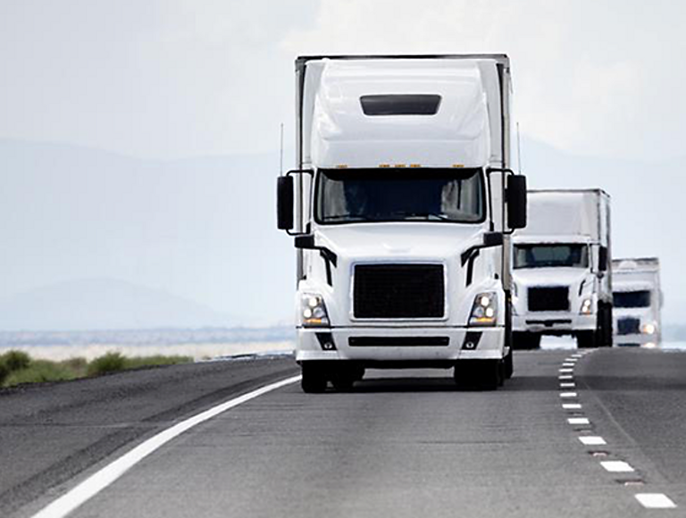 Three autonomous tractor trailers follow each other closely on the highway.