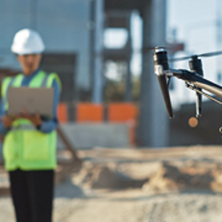Construction worker holds tablet while operating drone in front of him