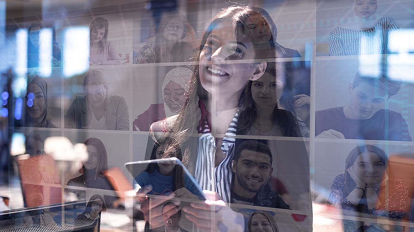 Smiling woman looks at screen with others video conferencing on it. Reflection of windows in background.
