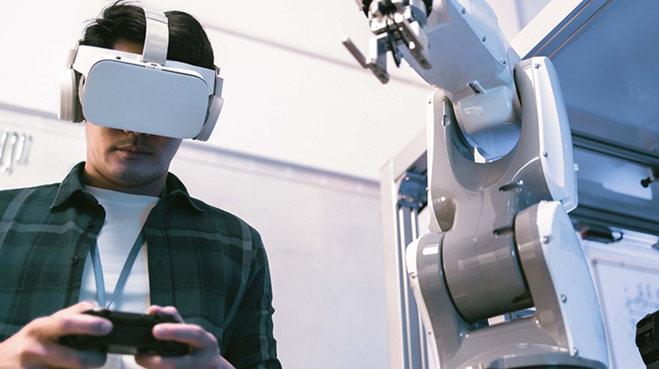 Student with VR headset stands with both hands on smart device.