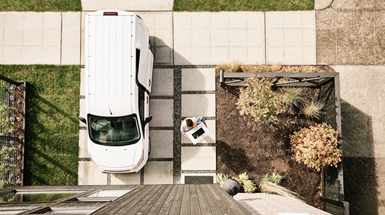 Overhead view of white delivery van outside home with woman carrying package to front door.