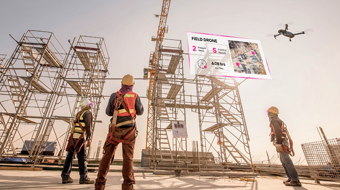 Three construction workers look skyward as one controls drone and virtual data appears in the sky