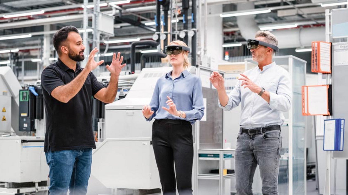 Person in an industrial setting instructs two other people while they’re wearing VR glasses